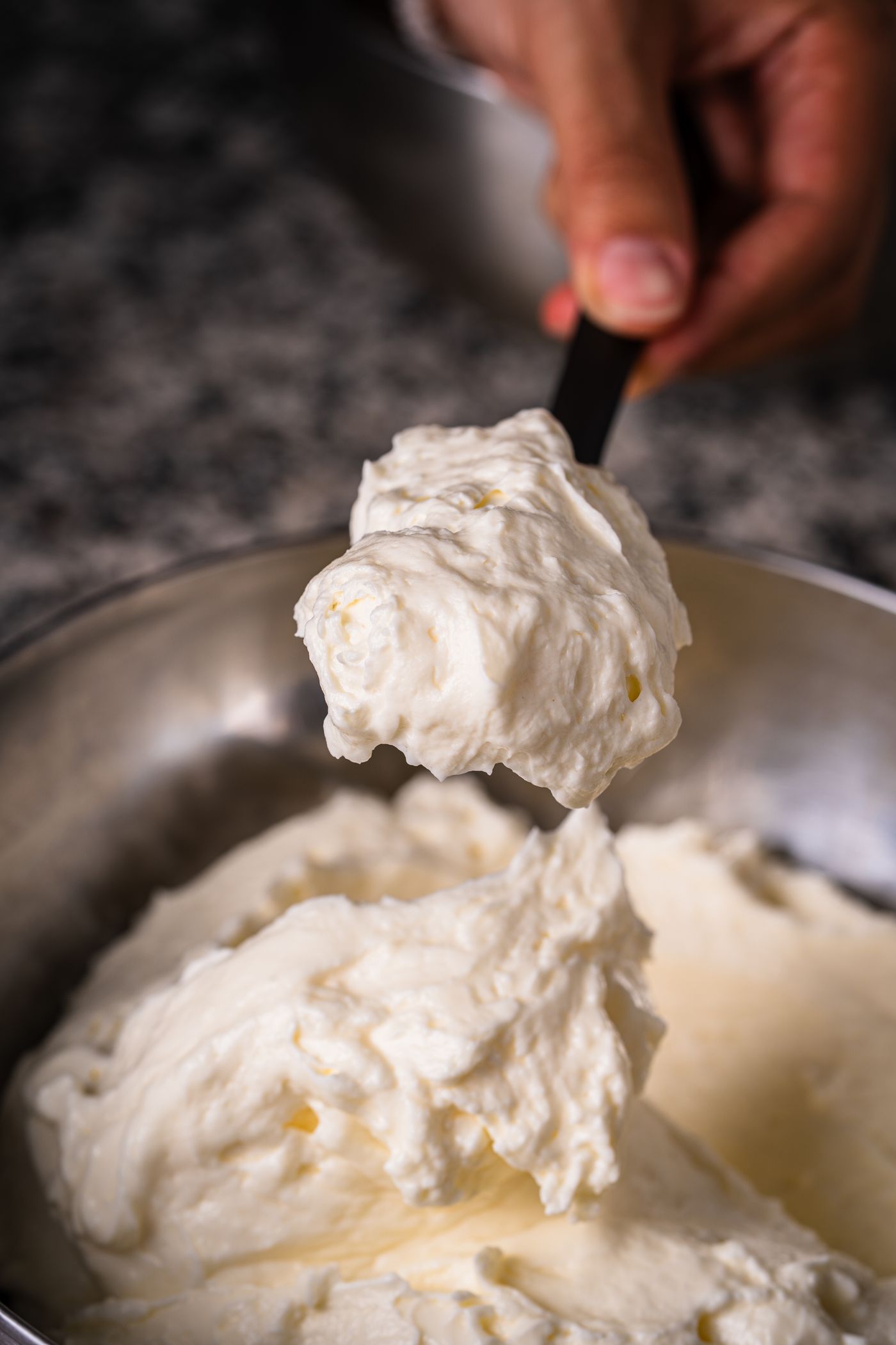 Creamy ricotta being worked in a metal bowl