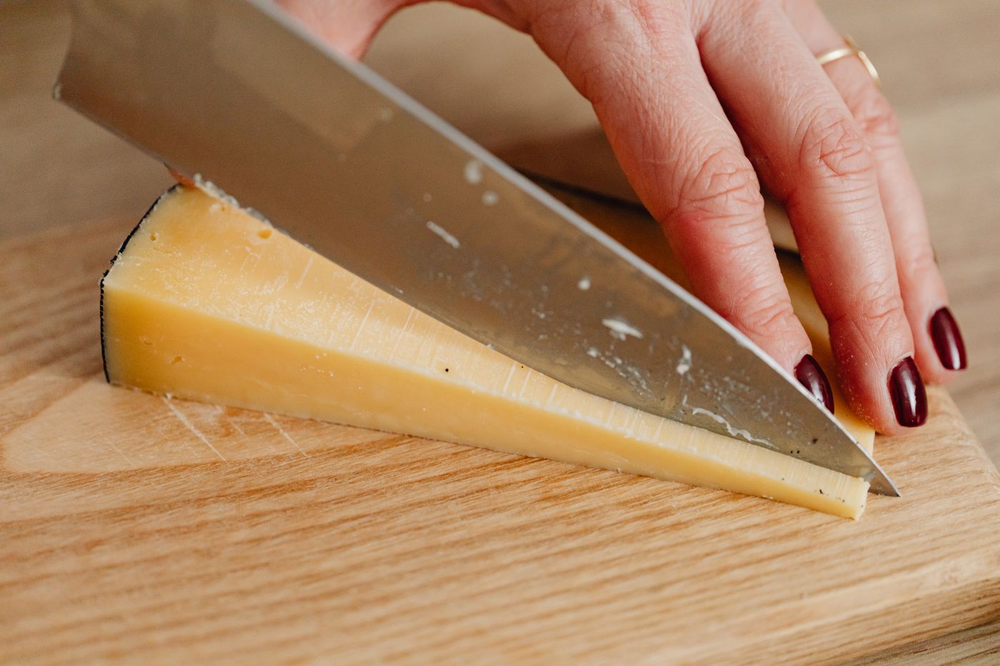 A knife cutting a hard cheese on a wooden board